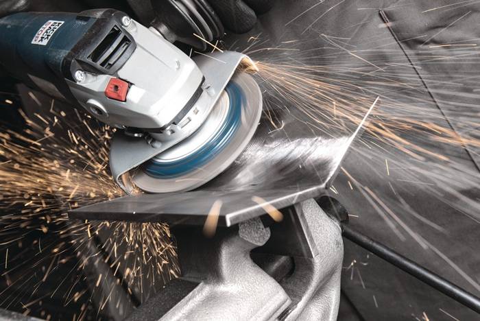 Eine Elektrowerkzeug, das ein Metallblech schneidet und helle Funken auslöst. Der Fokus liegt auf der Scheibe des Werkzeugs und dem geschwungenen Schnitt, der im Metall entsteht.
