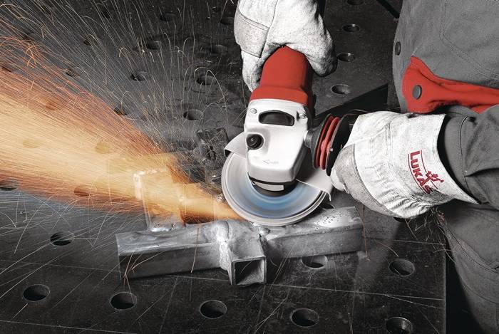 Eine Person mit Handschuhen verwendet eine Winkelschleifer, um ein Metallblech zu durchtrennen, wobei Funken in Richtung des Schnitts sprühen.