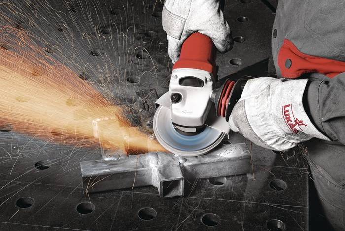 Eine Person mit Handschuhen verwendet einen Winkelschleifer, um Metall zu schneiden, wobei Funken auf einer gelochten Metalloberfläche entstehen.
