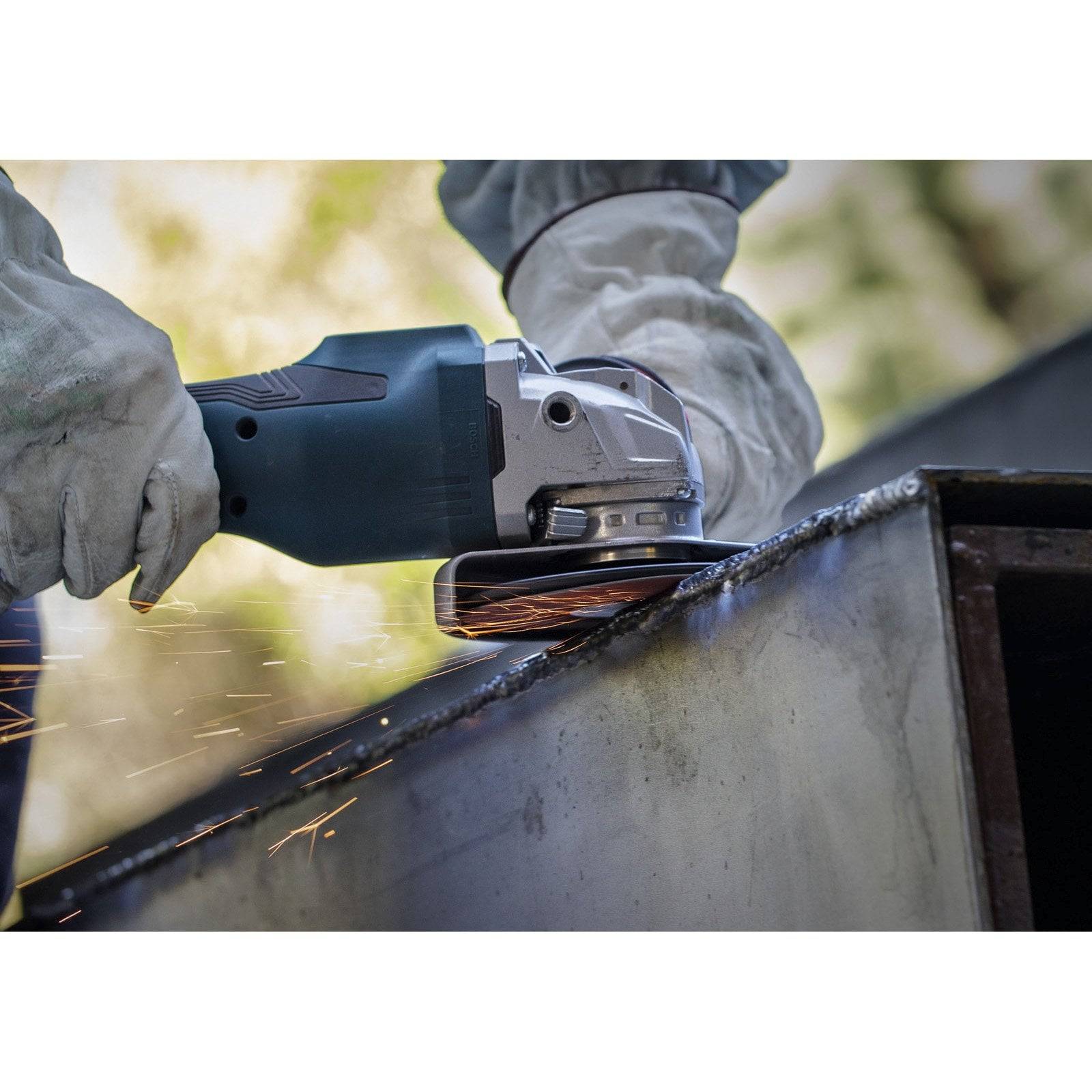 Eine Person mit Schutzhandschuhen verwendet eine Winkelschleifmaschine, die Funken aussendet, um die Kante einer Metalloberfläche zu glätten.