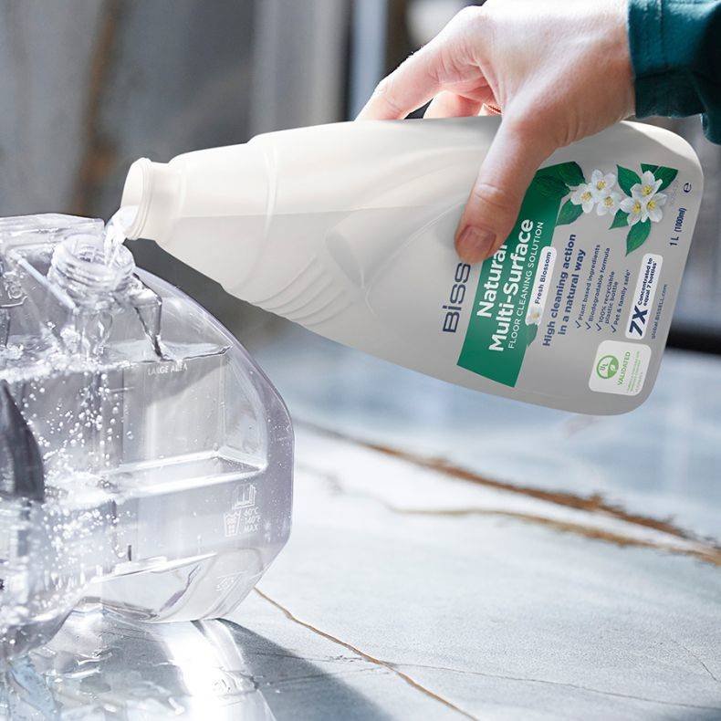 Eine Hand gießt transparente Flüssigkeit aus einer Biss Multiflächen-Reinigerflasche in einen Kunststoffbehälter.