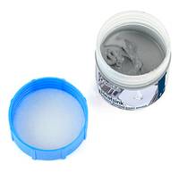 Offene Dose mit grauer Farbe mit blauem Kunststoffdeckel daneben auf weißem Hintergrund.