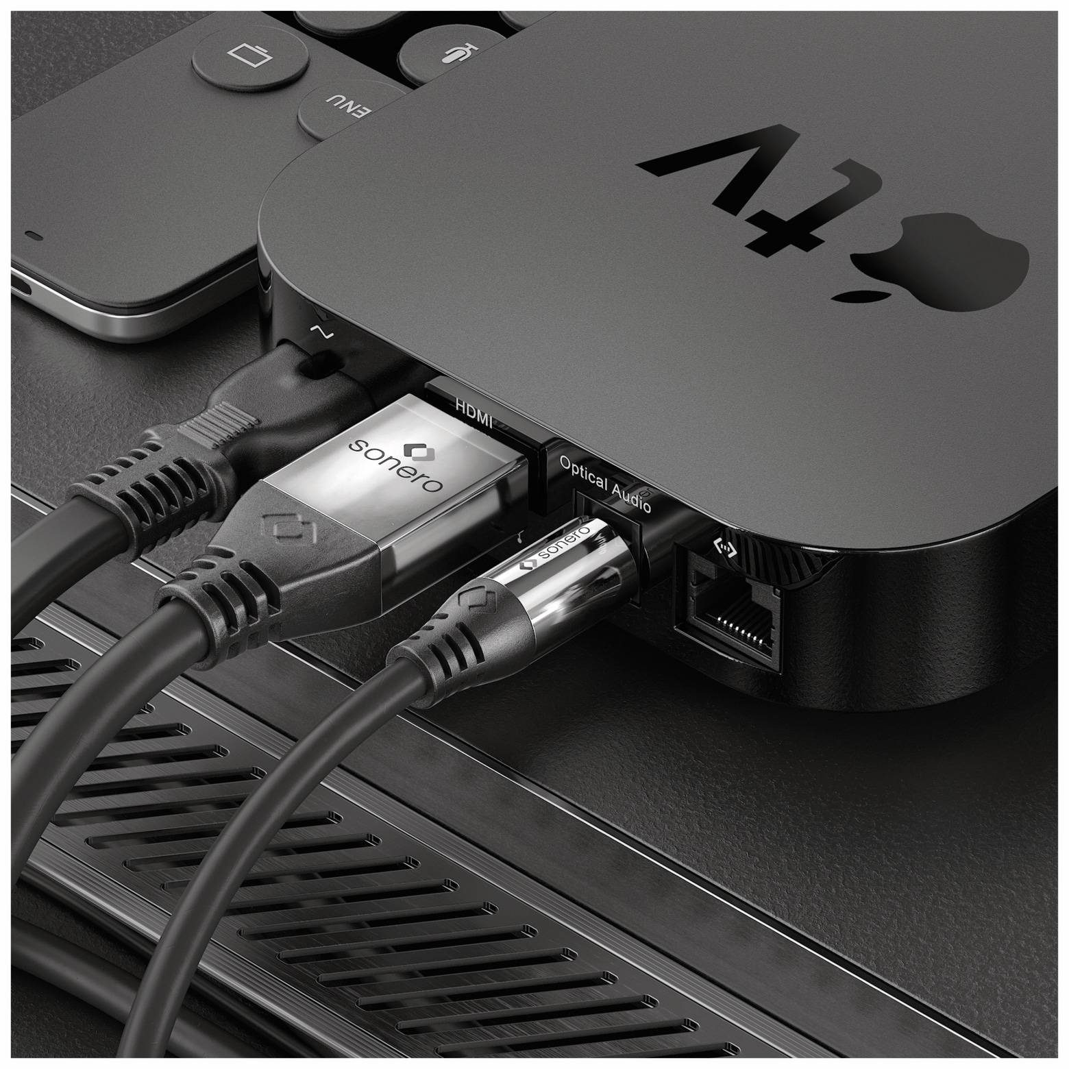 Nahaufnahme einer Apple TV 4K Box mit angeschlossenen HDMI- und Audiokabeln, die die Anschlüsse des Geräts und die teilweise sichtbare Fernbedienung zeigt.