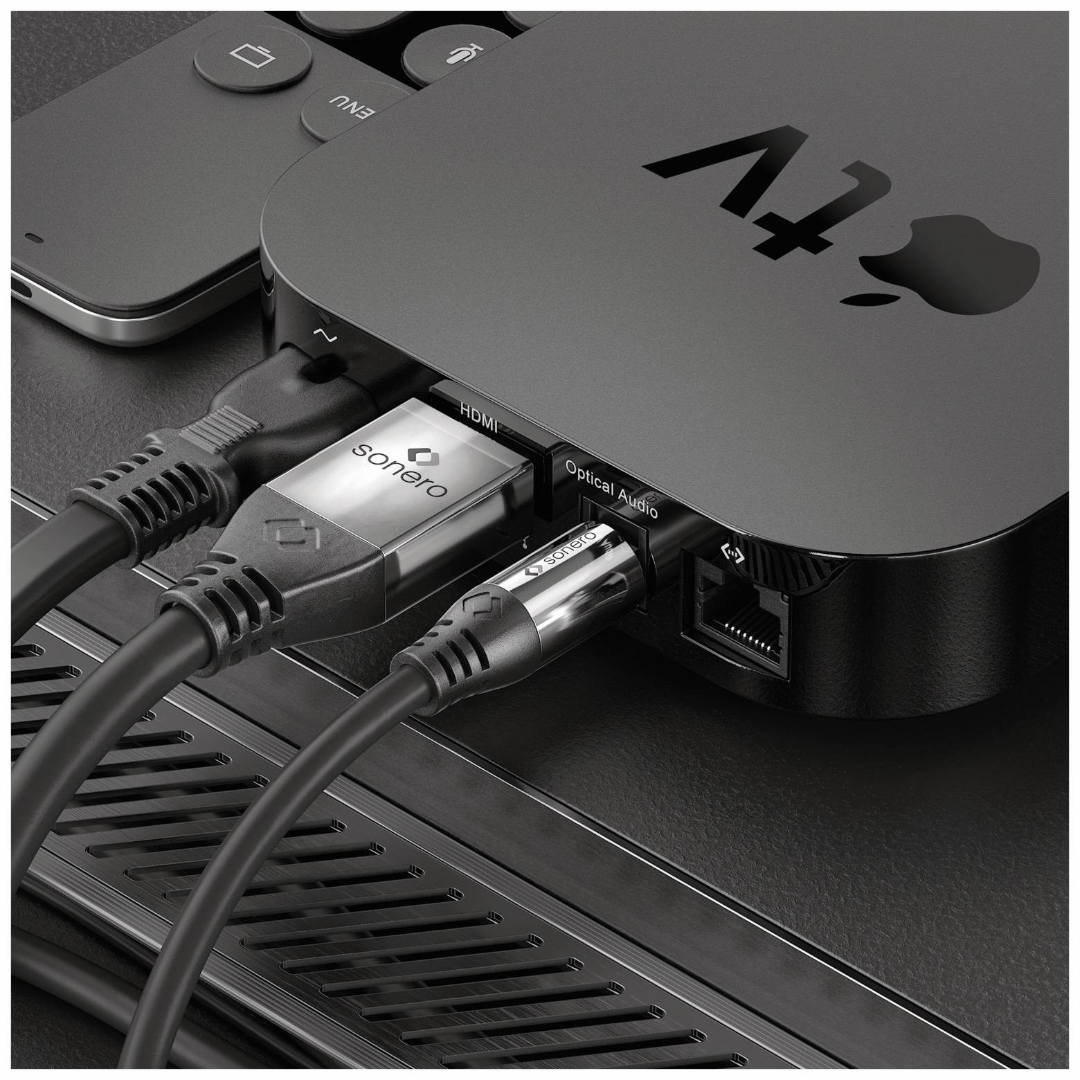 Nahaufnahme einer Apple TV Streaming-Box mit angeschlossenen HDMI-, Ethernet- und optischen Audiokabeln auf einer dunklen Oberfläche.