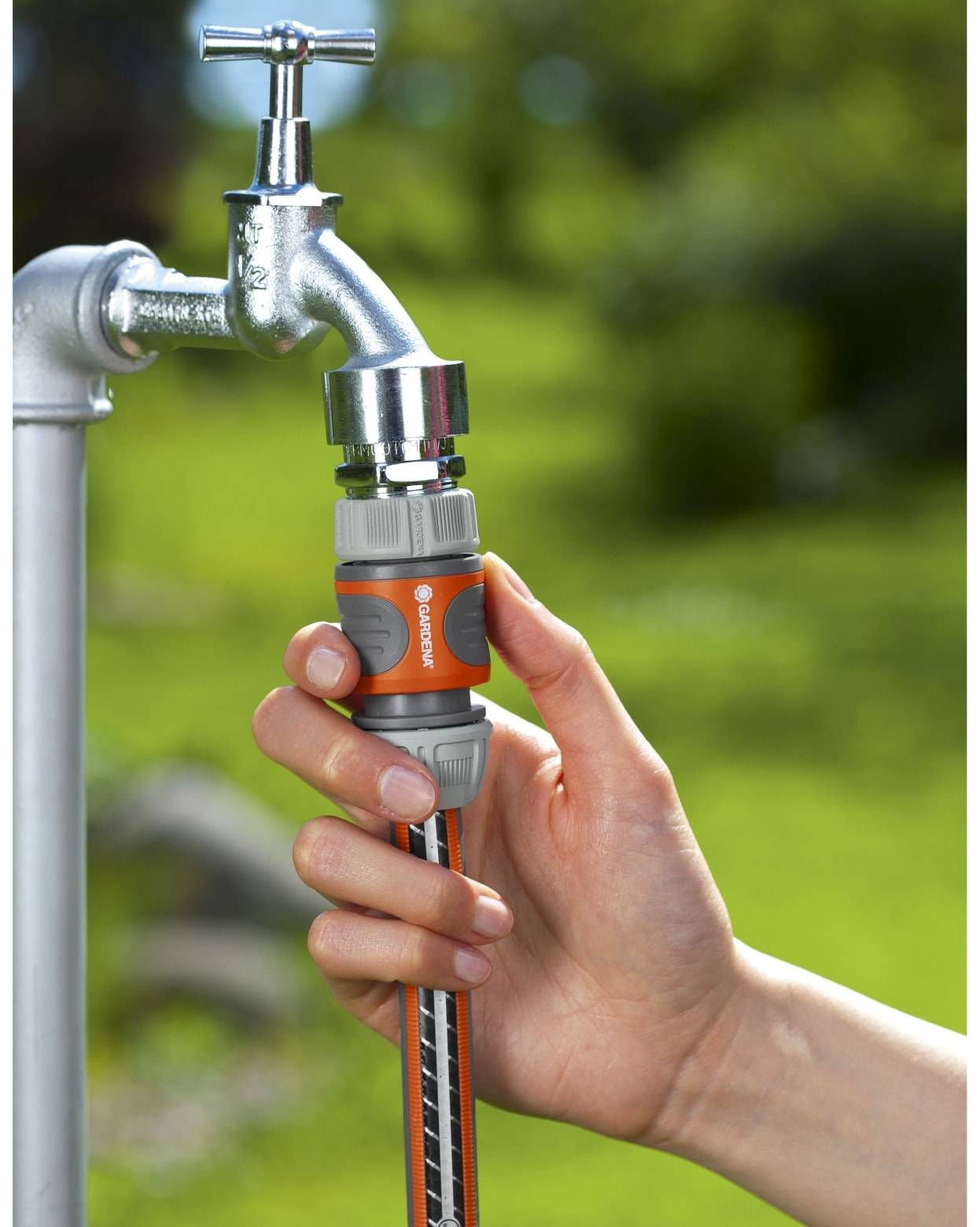 Hand, die einen Gartenschlauch mit einem Schnellkupplungsadapter an einen Außenwasserhahn anschließt, im Freien.