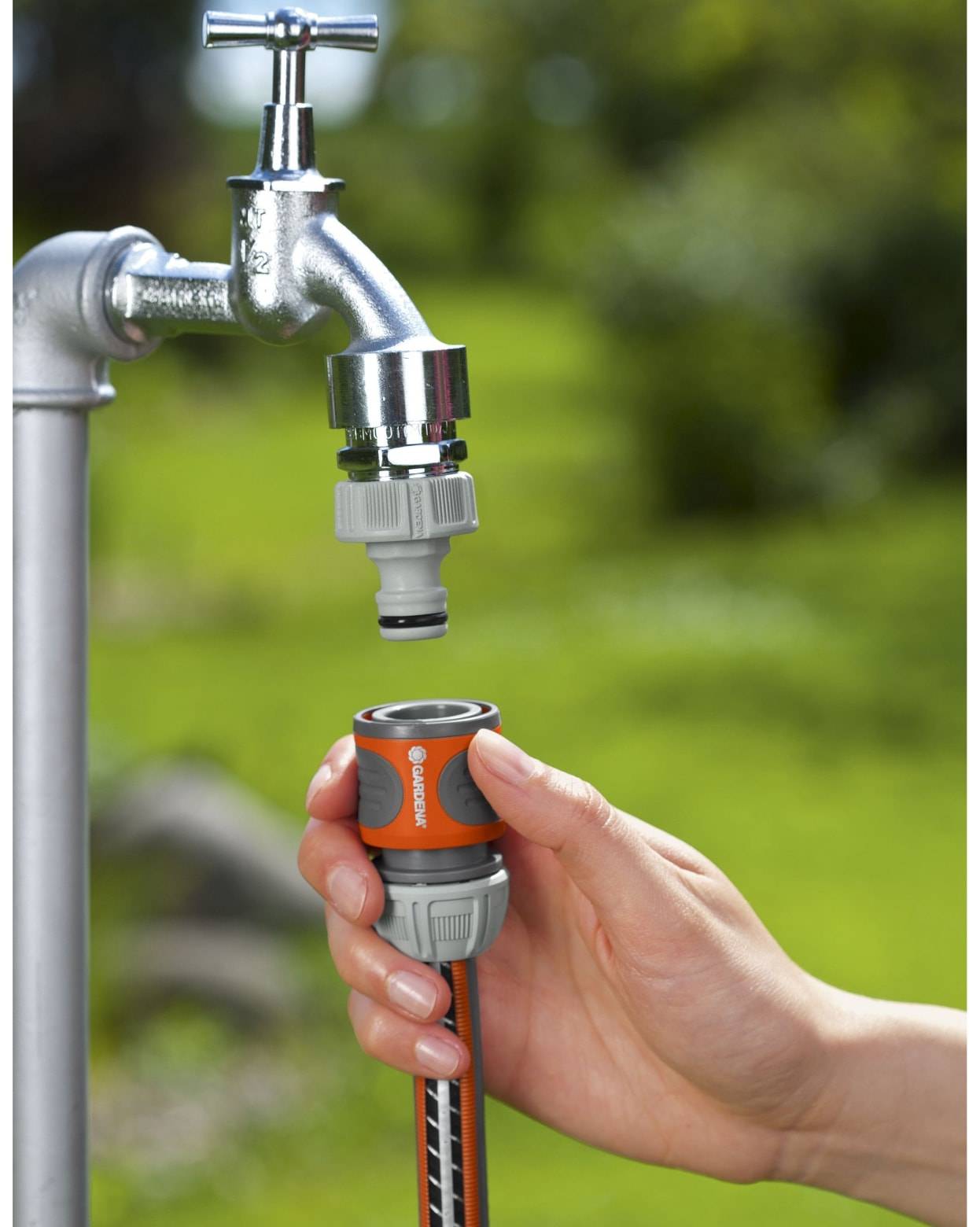 Eine Hand verbindet einen Gartenschlauch mit einem Außenwasserhahn mit einem Schnellverschlussstutzen und bereitet sich darauf vor, die Wasserzufuhr anzuschließen.