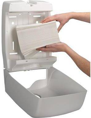 Hände, die einen Stapel Papier in einen an der Wand montierten Papiertuchspender mit offenem unteren Behälter einführen.