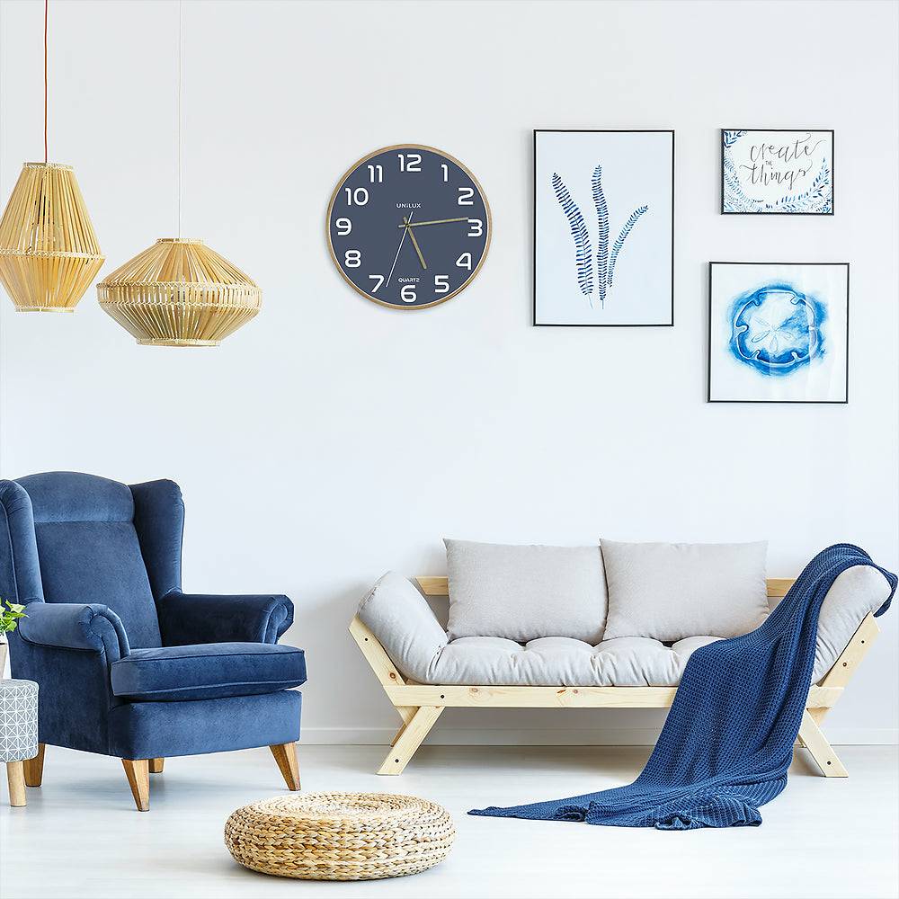 Helles modernes Wohnzimmer mit blauem Sessel, niedrigem beigefarbenem Sofa mit blauer Decke, geflochtenen Pendelleuchten, Wanduhr, Rahmenkunst und rundem Bodenkissen.