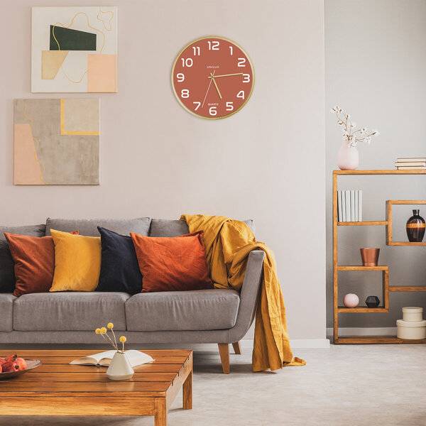 Modernes Wohnzimmer mit grauem Sofa, farbenfrohen Kissen und gelbem Plaid, Wanduhr, abstrakter Kunst, hölzernem Couchtisch und offenen Regalen.