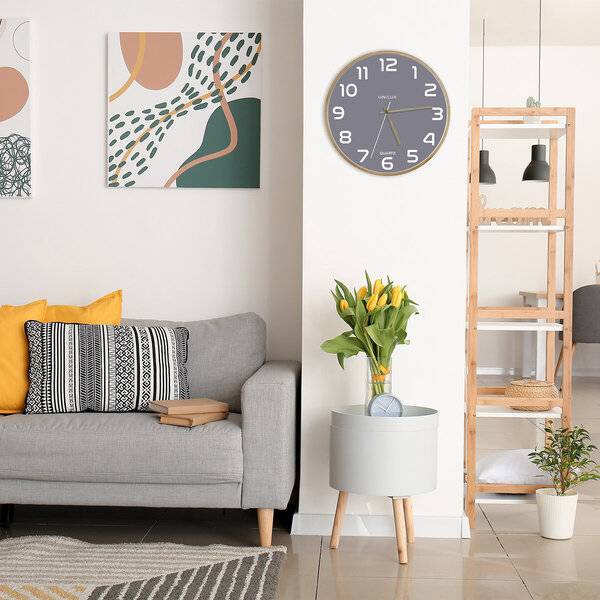Modernes Wohnzimmer mit grauem Sofa, abstrakter Wandkunst, Wanduhr, Lampenregal und Blumen auf einem Beistelltisch.