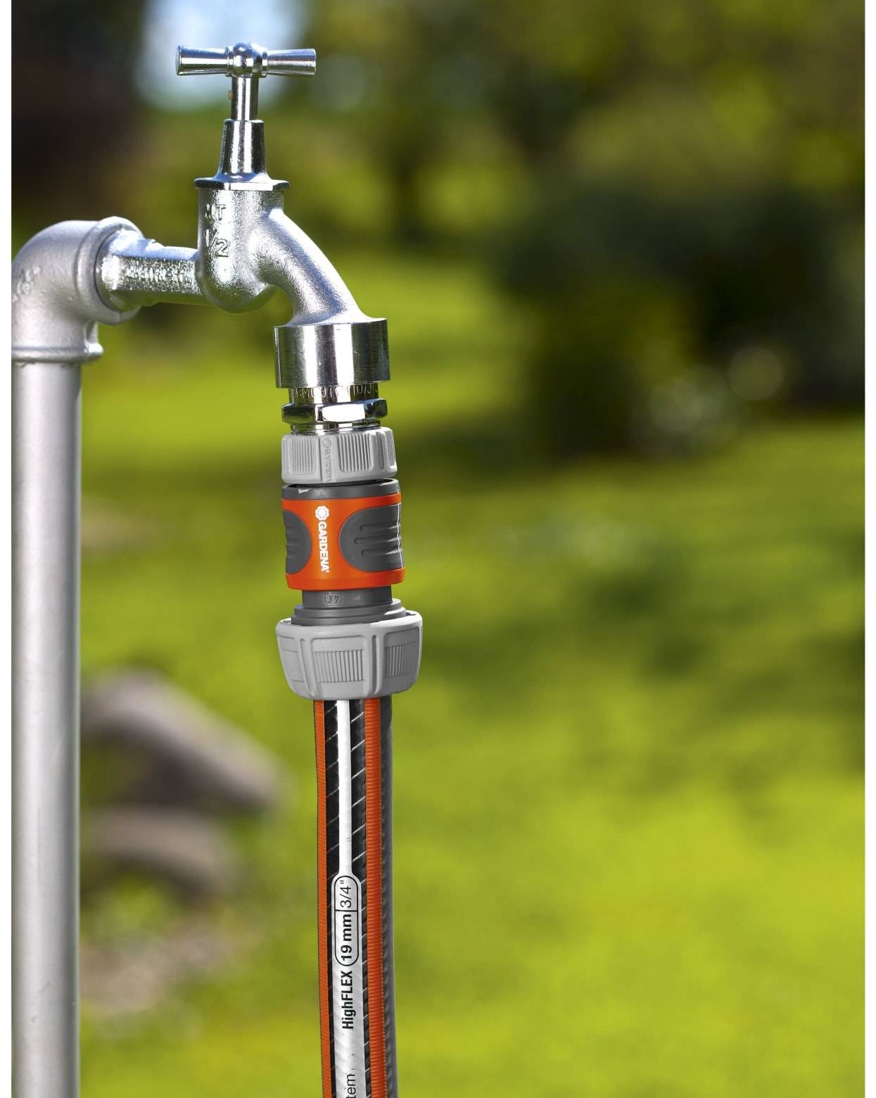 Ein Gartenschlauch, der mit einem Schnellverbinder an einem Metallwasserhahn im Freien angeschlossen ist, vor einem unscharfen grünen Rasengrund.