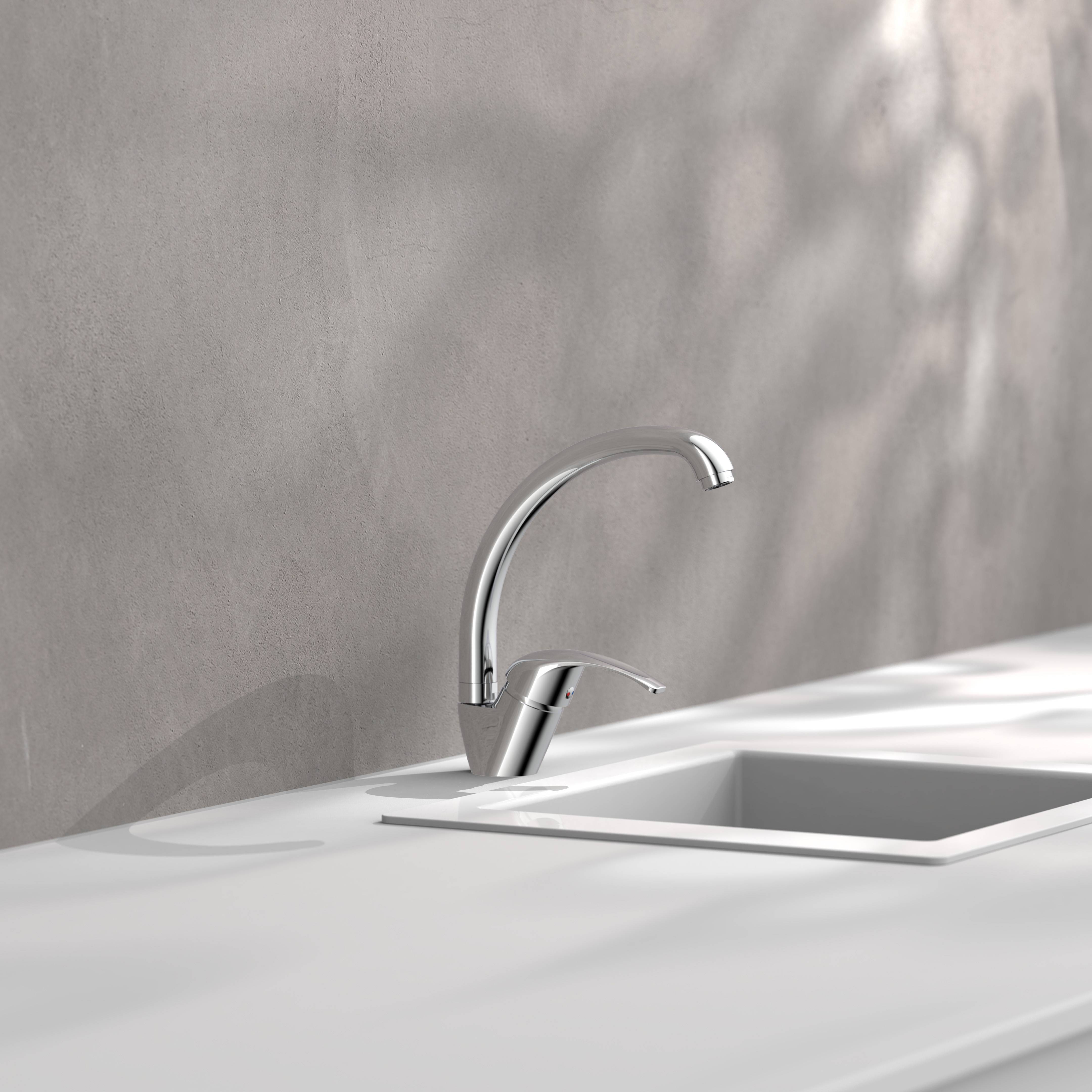 Moderner Chromkückenhahn neben einem weißen Spülbecken auf einer minimalistischen Arbeitsplatte montiert, mit weichem Licht und grauem Wandhintergrund.
