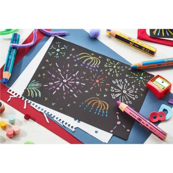 Bunte Feuerwerkszeichnungen auf schwarzem Papier, umgeben von Buntstiften, Bleistiften, einem Anspitzer und Bastelmaterialien auf einem weißen Tisch.