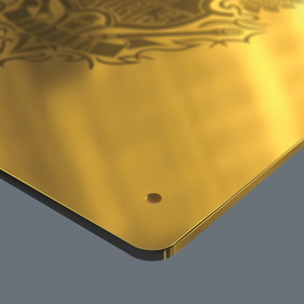 Eine Nahaufnahme einer metallischen Goldplakette mit kunstvollen Mustern und einem kreisrunden Loch in der Ecke, was auf eine mögliche Befestigungsmöglichkeit hindeutet.