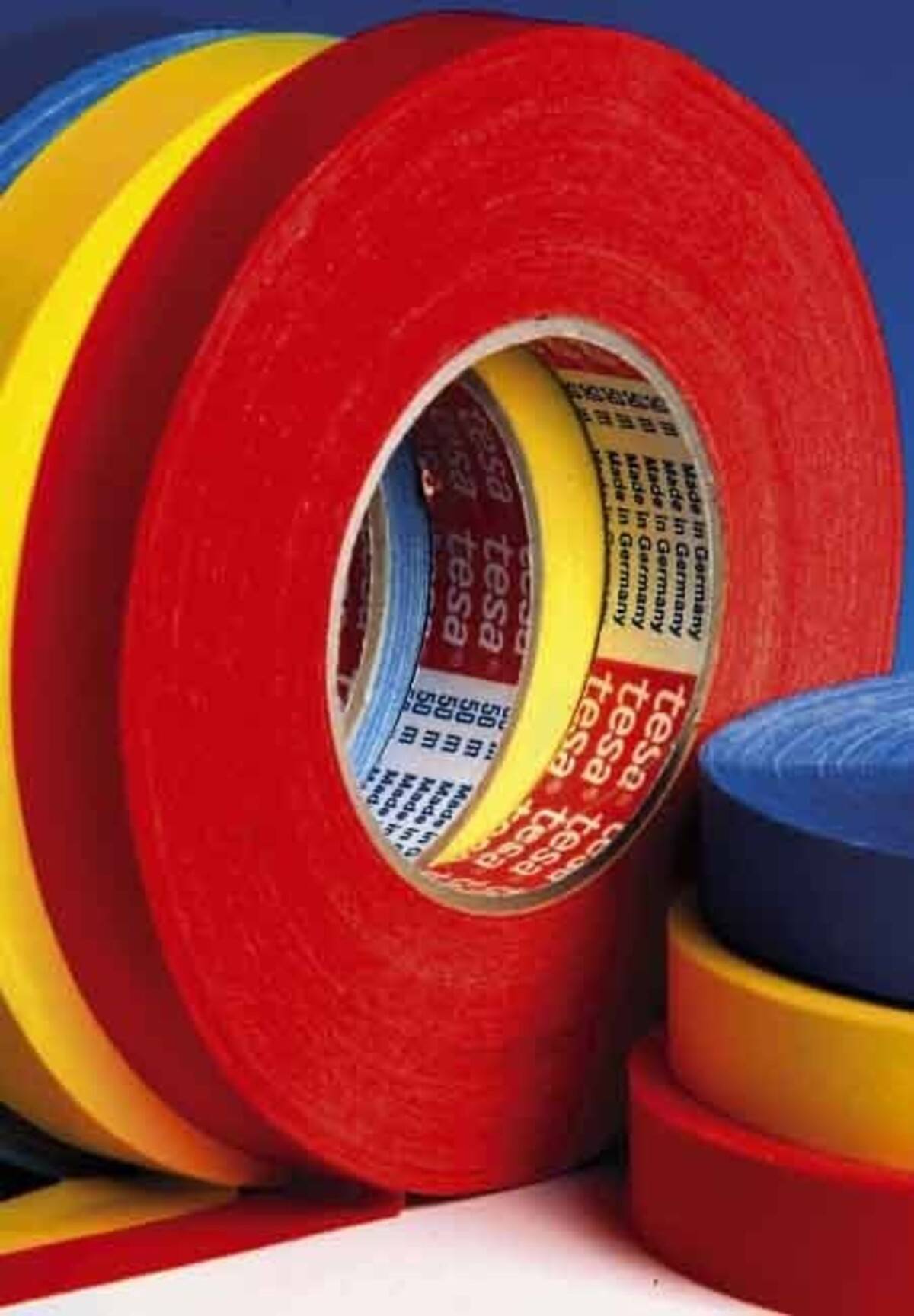 Gestapelte Rollen farbiges Klebeband, mit einer großen roten Rolle vorne und kleineren blauen, gelben und roten Rollen daneben.