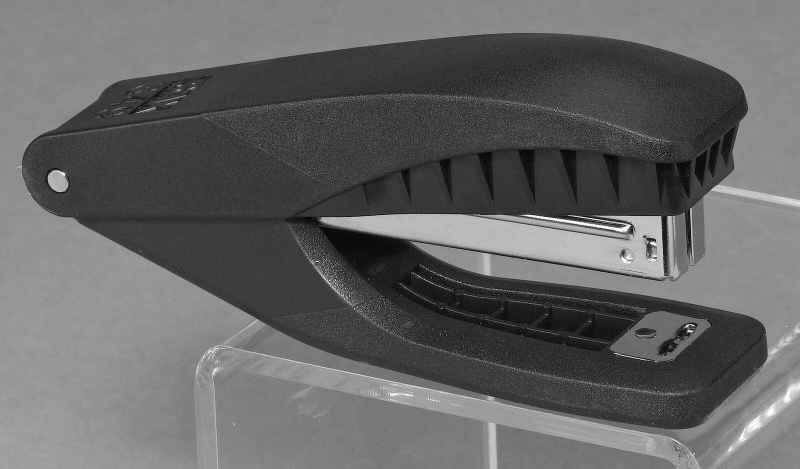 Ein schwarzer Heftklammern-Entferner mit silberner Metallspitze ruht auf einem transparenten Ständer vor einem grauen Hintergrund.