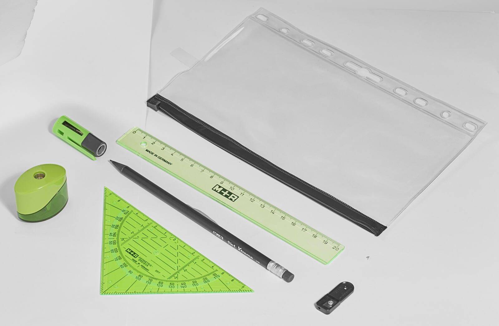 Ein durchsichtiger Kunststoffbeutel enthält einen grünen dreieckigen Winkelmesser, ein grünes Lineal, einen schwarzen Bleistift, einen Radiergummi und einen Bleistiftspitzer.
