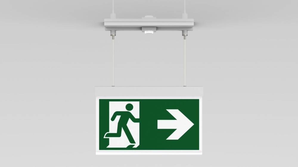 Ein grünes Notausgangsschild zeigt eine Figur, die durch eine Tür läuft, mit einem weißen Pfeil, der nach rechts zeigt und die Richtung zum Ausgang angibt.