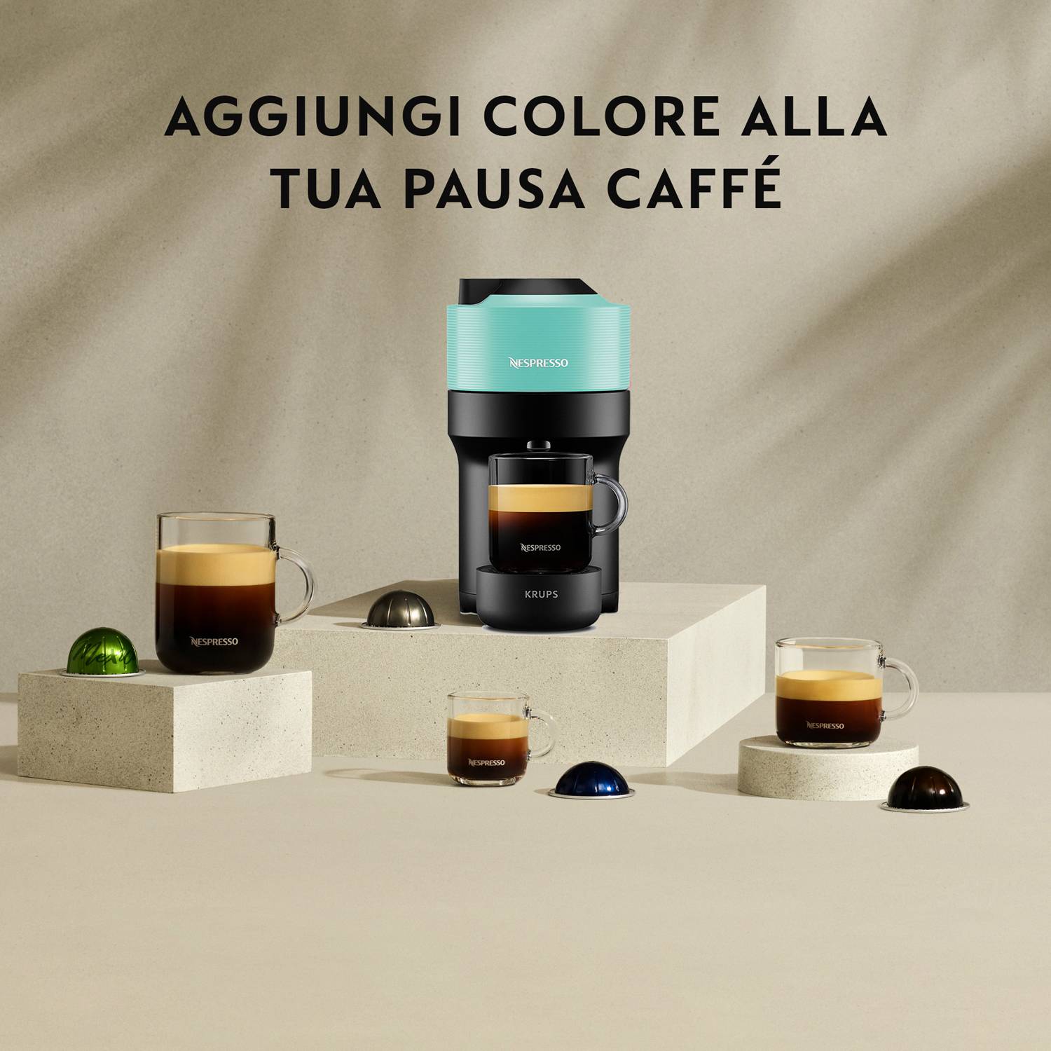 Nespresso-Kaffeemaschine auf einem Podest mit mehreren Kaffeegläsern, darunter das italienische Motto 'FÜGE FARBE DEINER KAFFEEPAUSE HINZU'.