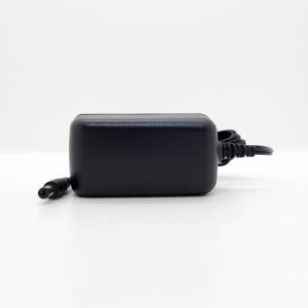 Ein schwarzes Netzteil mit einem Kabel ragt von der rechten Seite vor einem einfarbigen weißen Hintergrund hervor.