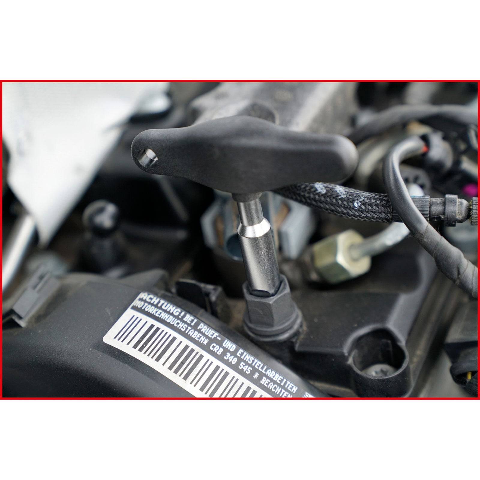 Ein Werkzeug wird in eine Komponente des Automotors eingeführt, was auf Wartung oder Reparatur hindeutet. Im Hintergrund sind Barcodes und Maschinen zu sehen.