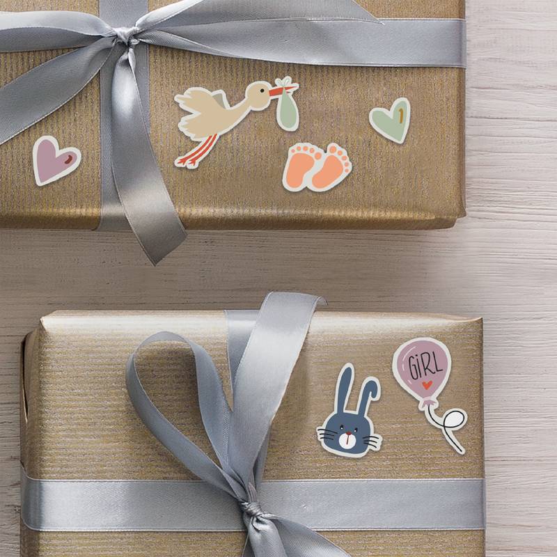 Zwei Geschenkkartons mit silbernen Bändern. Die obere Box hat Aufkleber mit Störchen und Babyartikeln. Die untere Box zeigt einen Hasen mit einem Sticker mit dem Ballon und dem Schriftzug 
