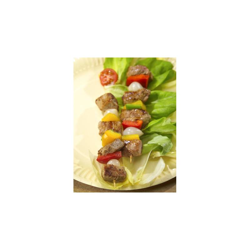 Spieße mit gegrilltem Fleisch, roten und gelben Paprikaschoten, Zwiebeln und Kirschtomaten auf einem Bett aus Salat, serviert auf einem beigen Teller.