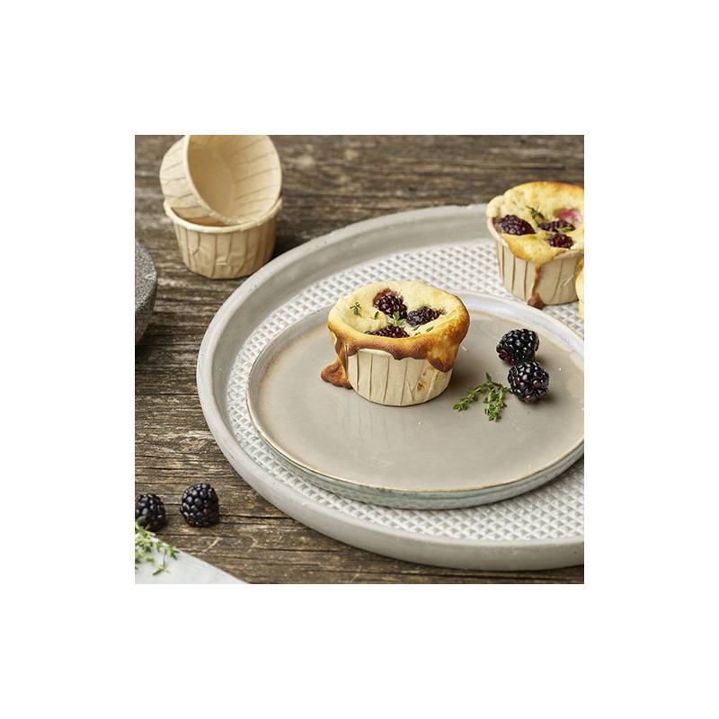 Muffin mit Brombeeren belegt auf einem Teller, umgeben von frischen Brombeeren und Thymiansprossen auf einem Holztisch.