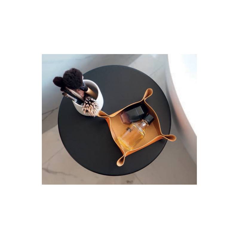 Ein schwarzer runder Tisch mit einem Ledertablett, das eine Parfümflasche und eine kleine schwarze Schachtel trägt. Ein silberner Behälter mit Make-up-Pinseln steht daneben.