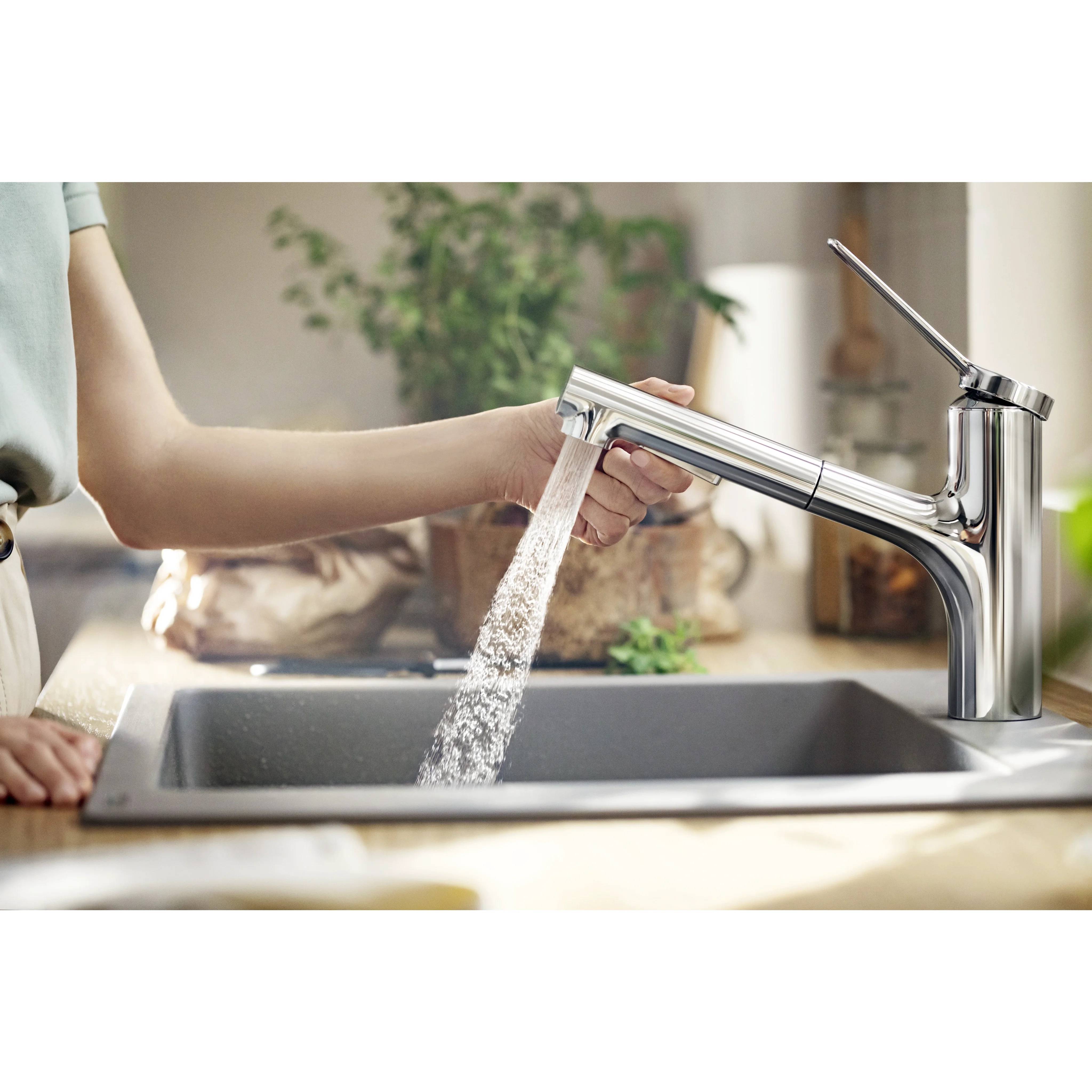 Person, die einen Wasserhahn in der Küche mit Wasser testet, das in ein Waschbecken fließt, zeigt einen modernen Chromwasserhahn in einer Heimatküche.
