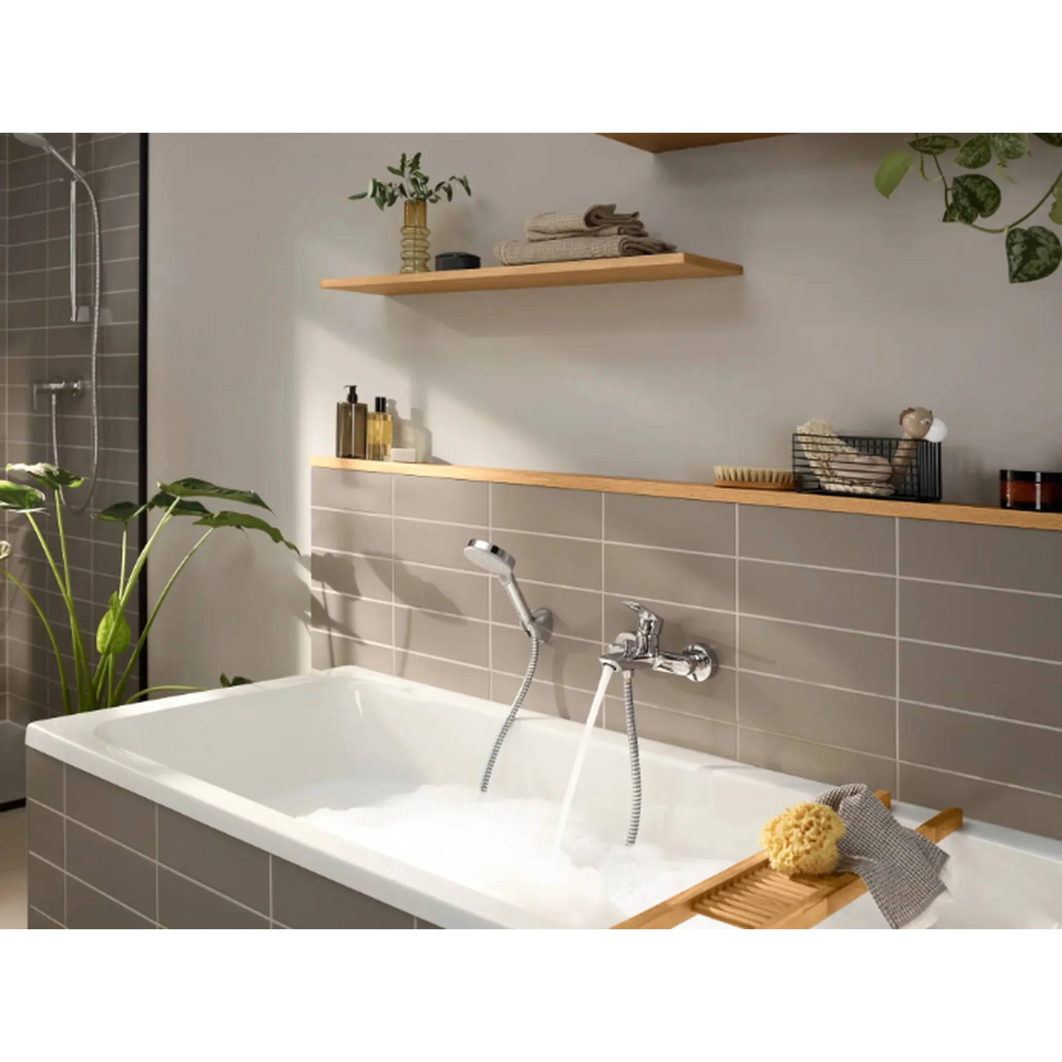 Modernes Badezimmer mit einer weißen Badewanne, verchromtem Wasserhahn und Brauseschlauch, beiger Fliesenwand, Holzregalen mit Toilettenartikeln und einer Pflanze in der Nähe.