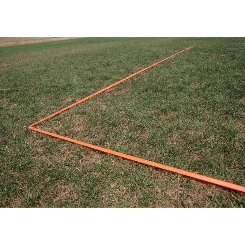 Zwei lange, sich kreuzende orangefarbene Maßbänder liegen auf einem Grassland und bilden einen Winkel, was auf eine Vermessungs- oder Layoutaktivität hindeutet.