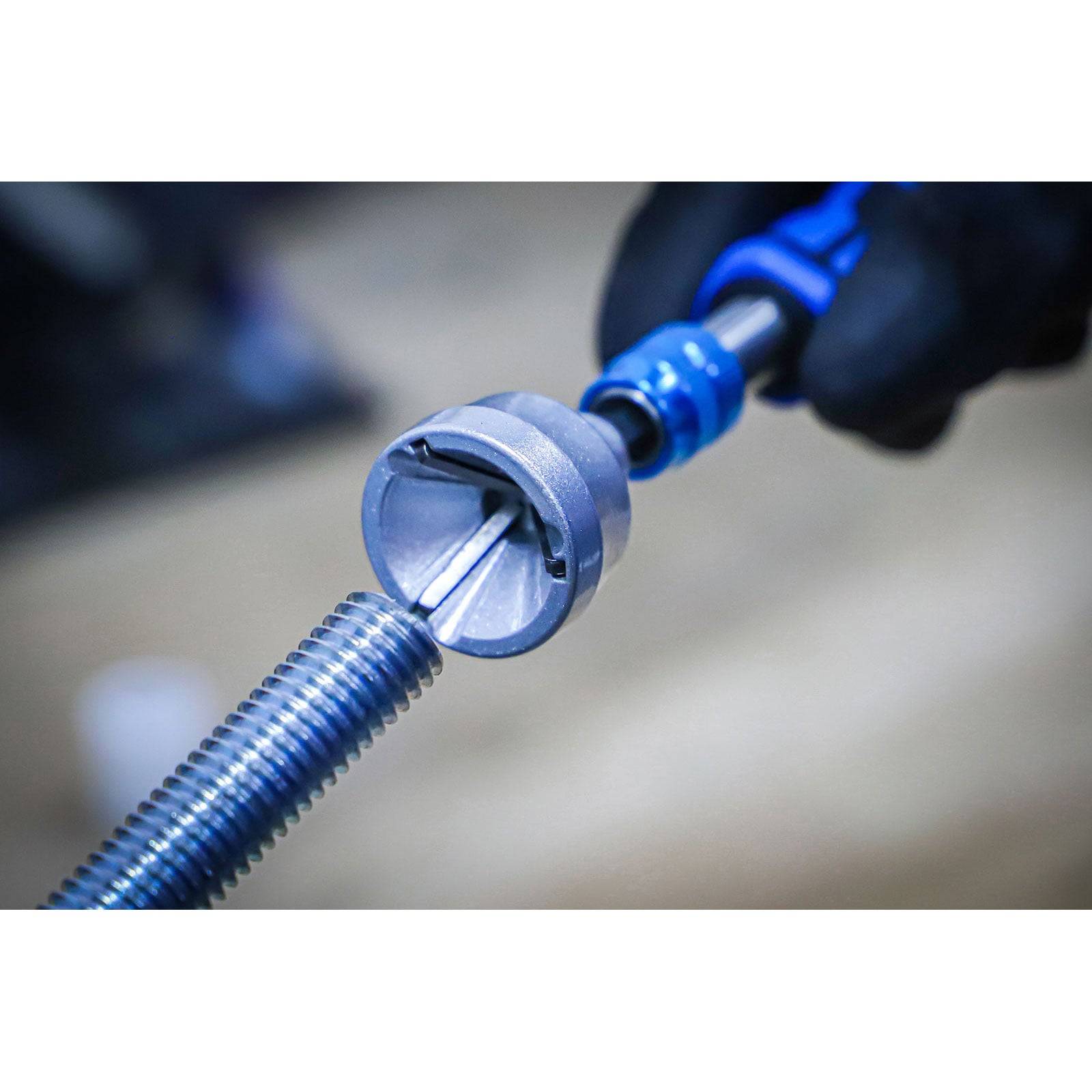 Eine Person benutzt ein Entgratungswerkzeug, um die Kante einer Gewindestange zu glätten. Der Hintergrund ist unscharf, wobei das Werkzeug im Einsatz im Fokus steht.