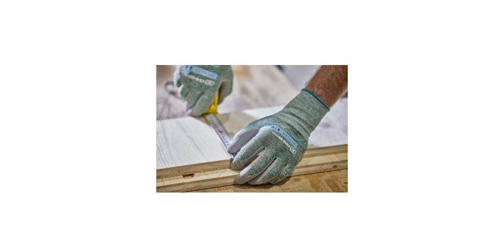 Eine Person mit Handschuhen misst eine Holzplanke mit einem Bandmaß auf einer Werkbank und deutet damit auf eine Zimmermanns- oder Heimwerkeraktivität hin.