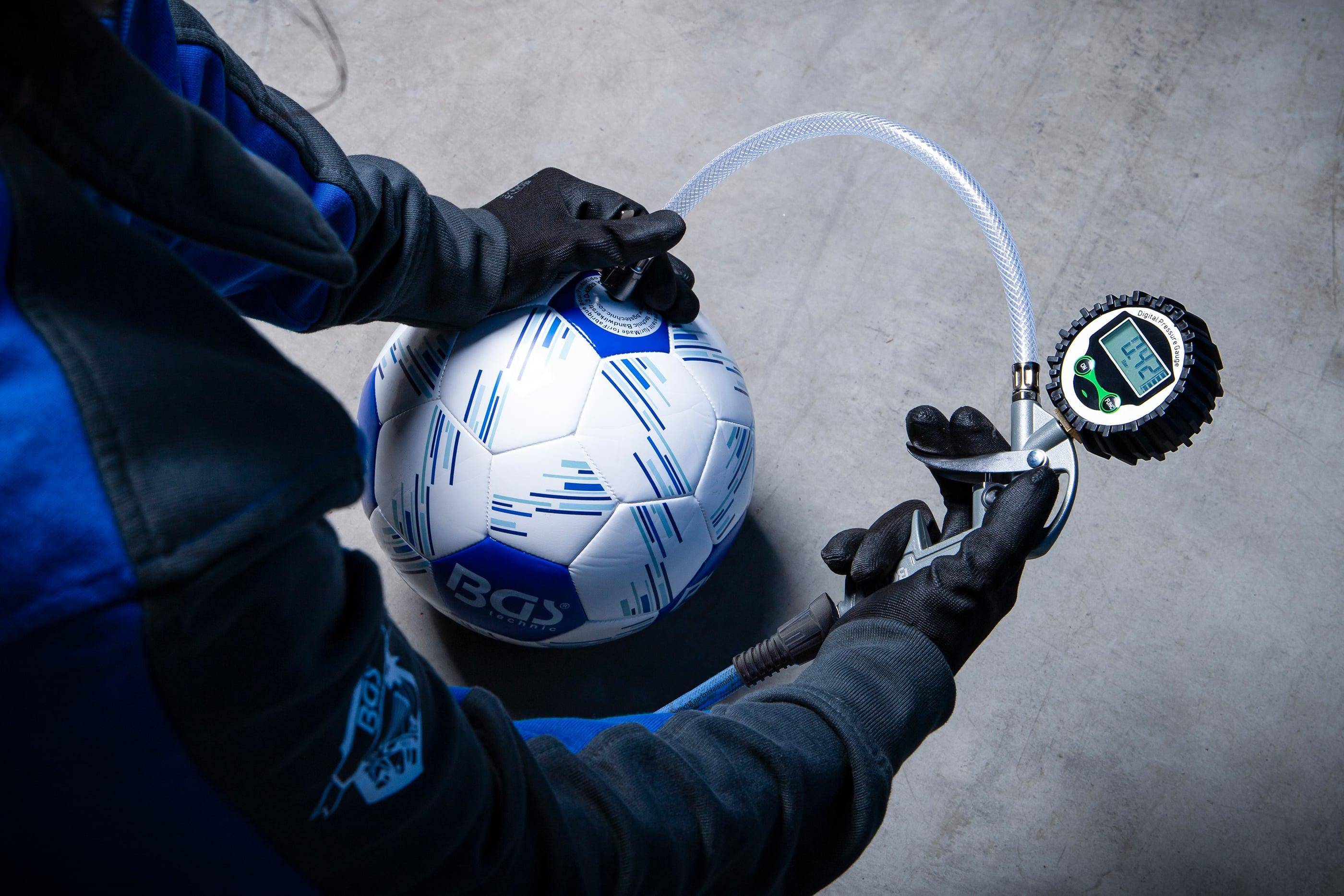 Eine Person in Handschuhen benutzt eine Pumpe, um einen blau-weißen Fußball auf einem Betonboden aufzupumpen.
