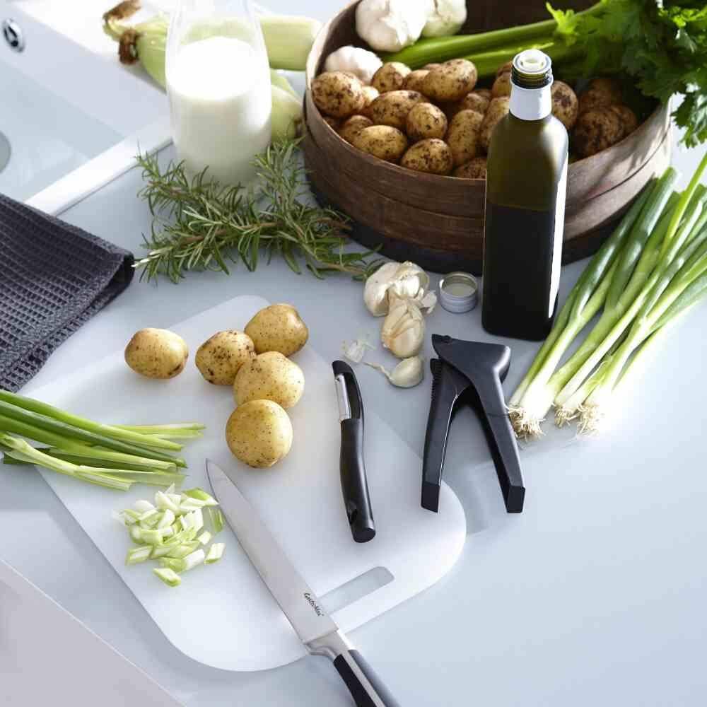 Eine Küchenarbeitsplatte zeigt Kartoffeln, Frühlingszwiebeln, Knoblauch, Rosmarin, Olivenöl, ein Glas Milch und Küchenutensilien, bereit zum Kochen.