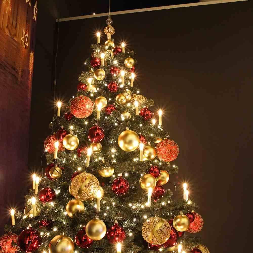 Ein geschmückter Weihnachtsbaum mit leuchtenden Lichtern, roten und goldenen Christbaumkugeln in einem dämmrigen Raum, der eine festliche Atmosphäre schafft.