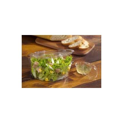 Eine Plastikschale mit Salat, bestehend aus Grünblättern, Mais und Schinken auf einem Holztisch, im Hintergrund begleitet von geschnittenem Brot.