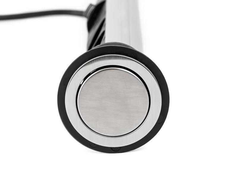 Eine silberne Taste auf einer zylindrischen Oberfläche, möglicherweise Teil einer einziehbaren Steckdose mit einem schwarzen Kabel, das aus der Rückseite herausragt.