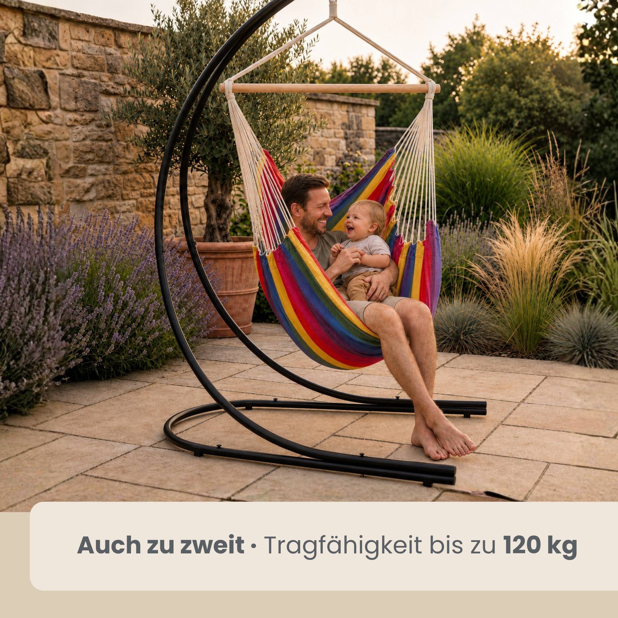 Mann und Baby sitzen zusammen in einem Regenbogen-Hängesessel im Freien; Text sagt „Auch zu zweit · Tragfähigkeit bis zu 120 kg