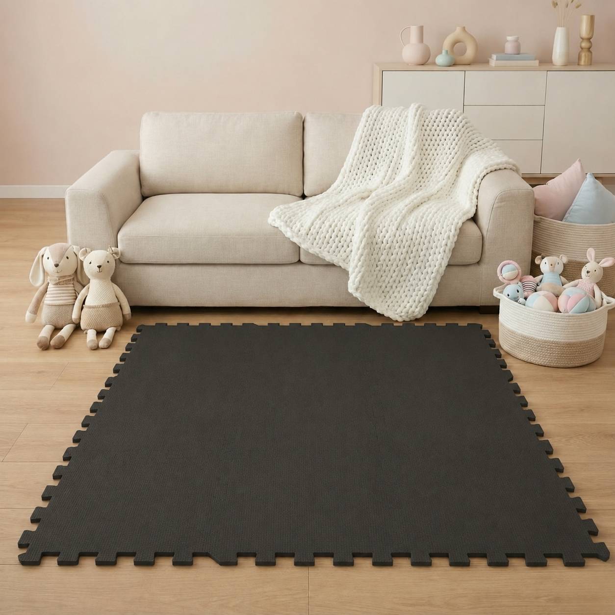 Schwarze verschlungene Schaumstoff-Spielmatte auf einem Holzboden in einem kinderzimmerähnlichen Wohnzimmer mit beigem Sofa, Spielzeugen und Aufbewahrungskörben.