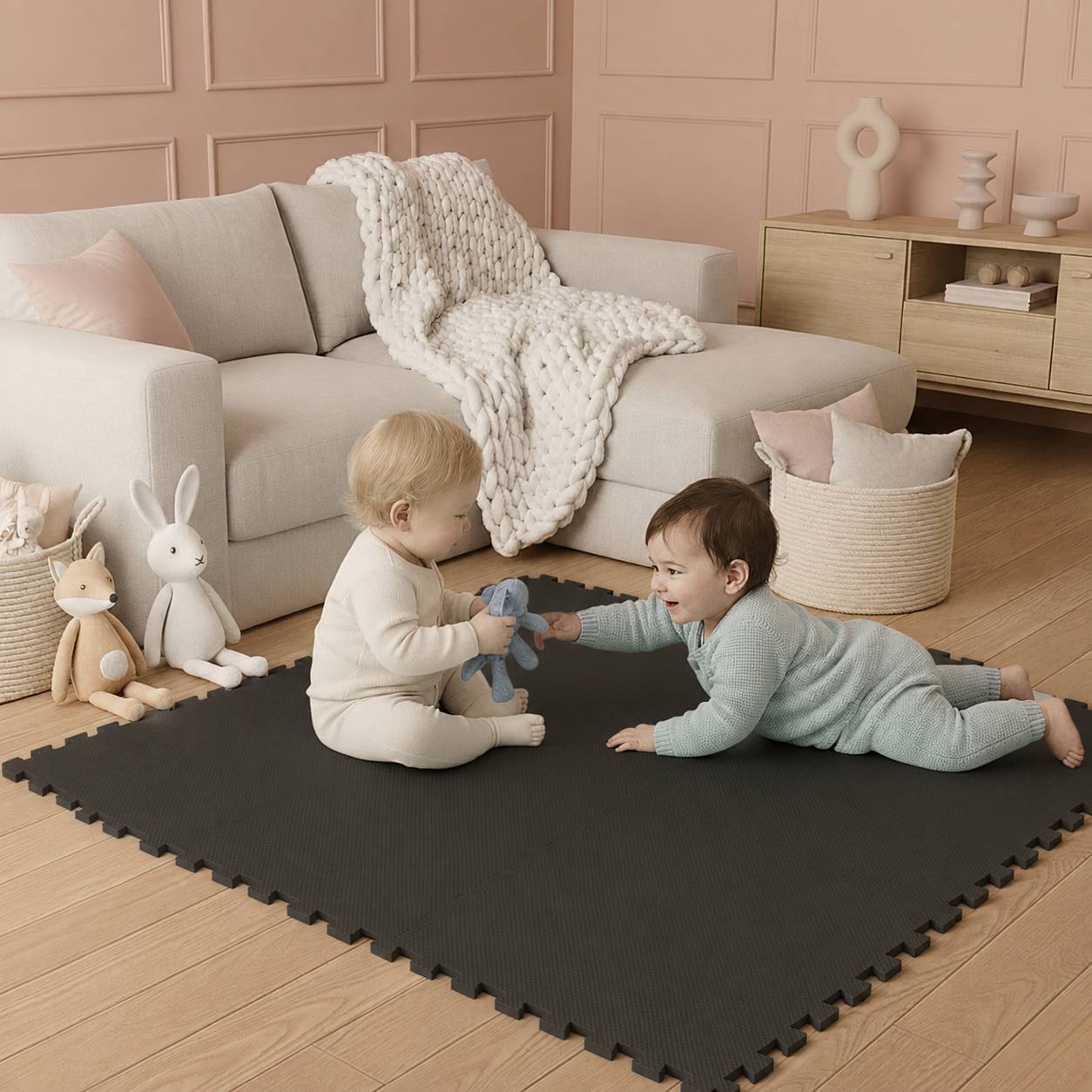 Zwei Kleinkinder spielen auf einer schwarzen Schaumstoffmatte in einem Wohnzimmer in Pastelltönen und sitzen neben einem beigen Sofa mit Stoffhasen und einem Spielzeug in der Hand.