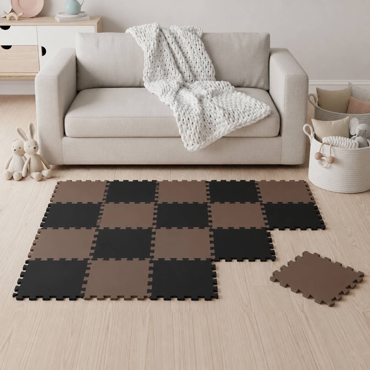 Beige-Sofa in einem kinderfreundlichen Wohnzimmer mit einer gestrickten Wurfdecke, Spielzeughasen und verschachtelten Schaumstoffmatten, die in einem teilweise verlegten Gittermuster angeordnet sind.