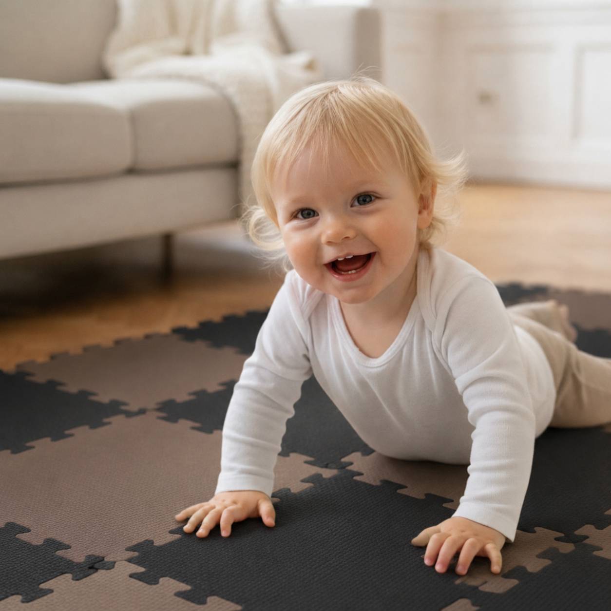 Ein lächelndes Baby krabbelt auf einer Schaumstoff-Spielmatte in einem hellen Wohnzimmer neben einem Sofa.