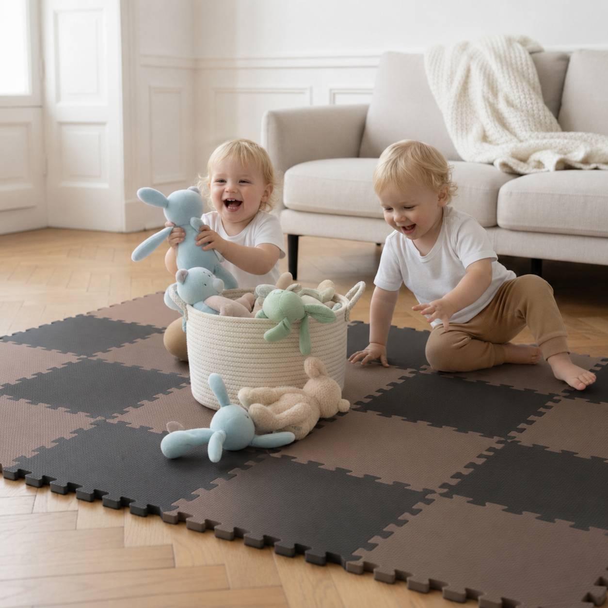Zwei Kleinkinder spielen auf einer Schaumstoffmatte neben einem Sofa, lächeln, während sie Kuschelhasenpuppen aus einem Korb in einem hellen Wohnzimmer sortieren.