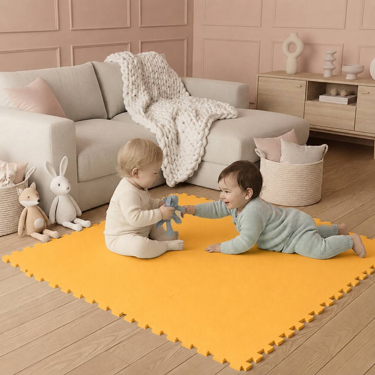 Zwei Babys spielen auf einer leuchtend orangefarbenen Schaumstoffmatte in einem wohnzimmerähnlichen Kinderzimmer, mit einem Sofa, einer Decke und Stoffhasen in der Nähe.