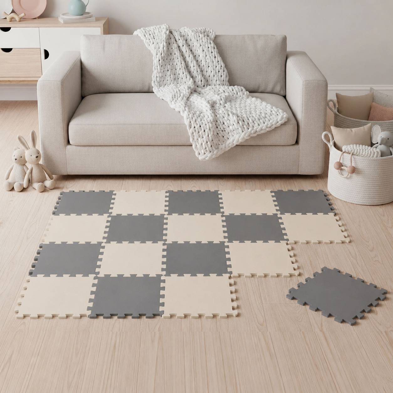 Gemütliches Wohnzimmer mit einem beigen Sofa, gestrickter Wurfdecke und grau-cremefarbener Schaumstoff-Spielmatte auf dem Boden; Spielzeugkaninchen und Körbe in der Nähe.