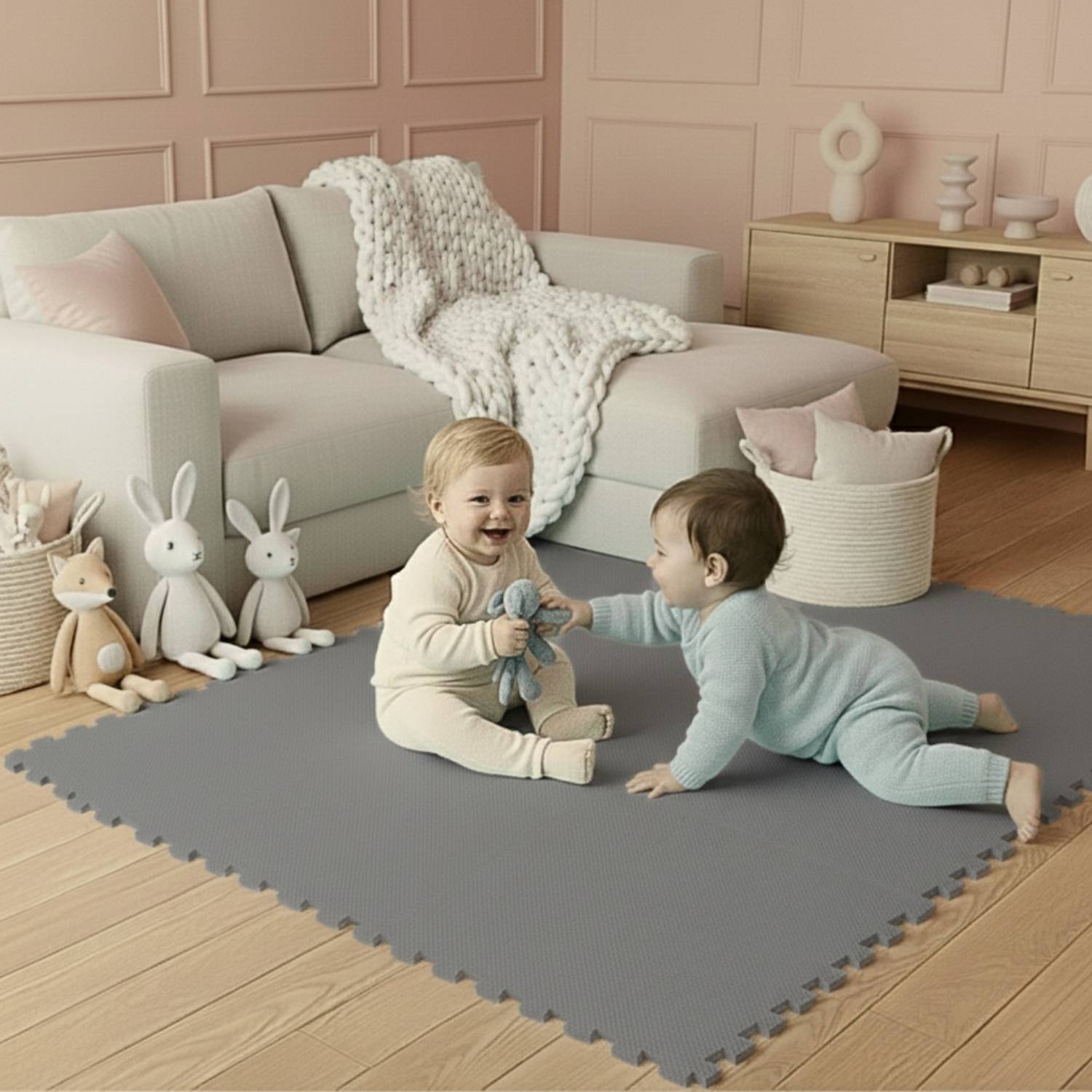 Zwei Kleinkinder sitzen auf einer grauen Spielmatte in einem gemütlichen, pastellfarbenen Wohnzimmer, umgeben von kuscheligen Spielzeugen und einem Sofa im Hintergrund.