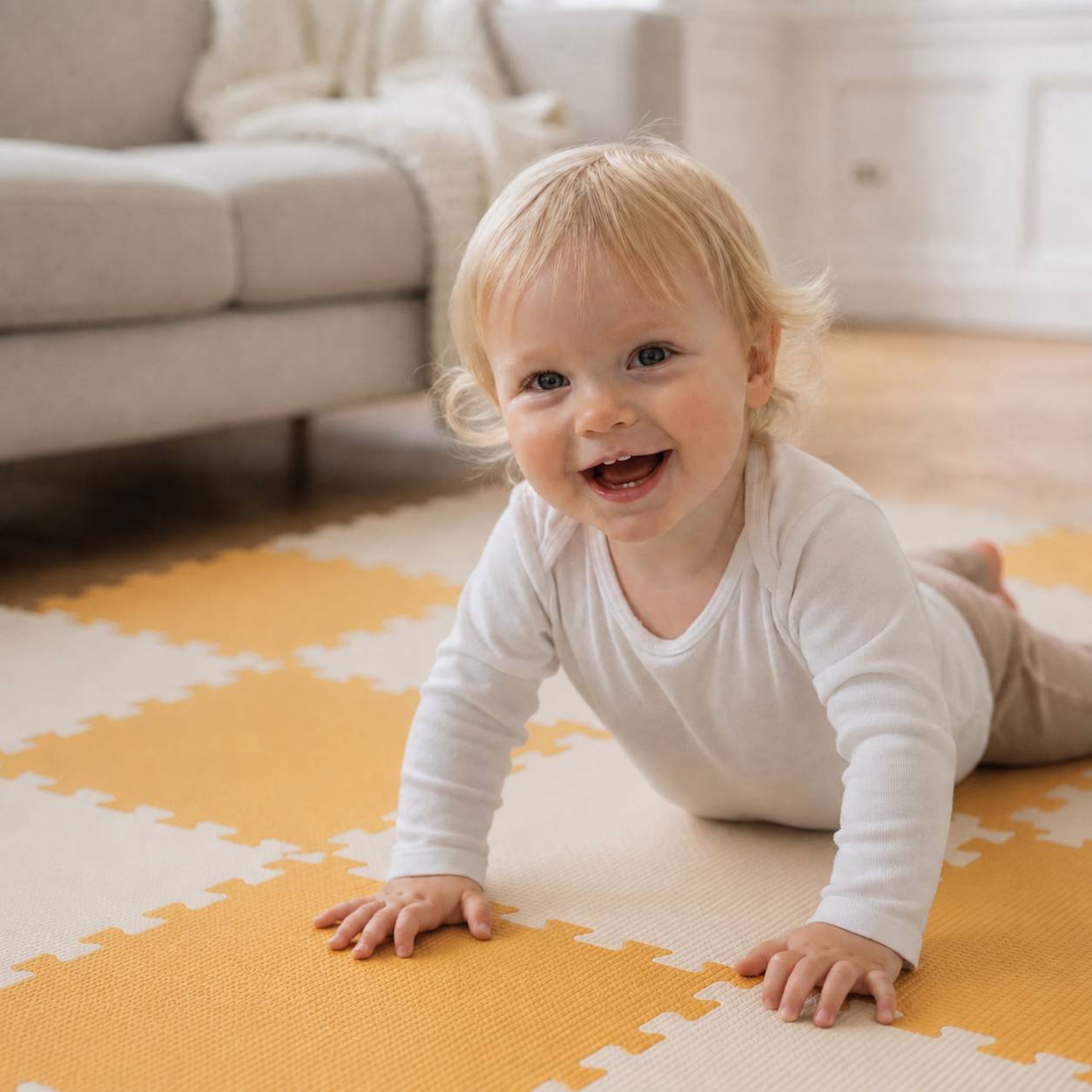 Lächelndes Baby in weißem Outfit, das auf einer gelb-weißen Spielmatte in einem hellen Wohnzimmer krabbelt.