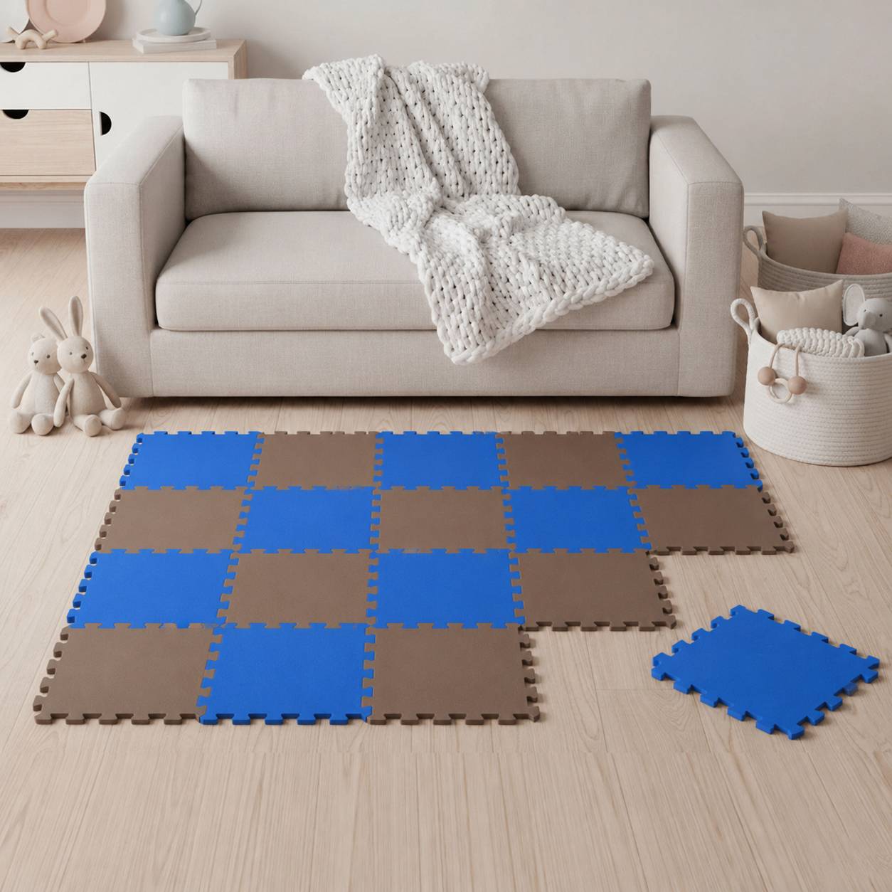Wohnzimmer mit beigem Sofa und gestrickter Wurfdecke; blau und braun gefärbte Schaumstoff-Puzzlemattenkacheln auf dem Boden verteilt, mit einer zusätzlichen Kachel zur Seite.